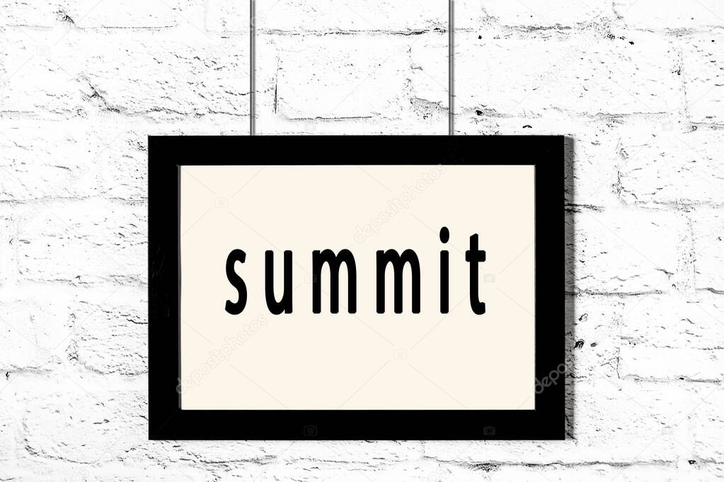 Black frame hanging on white brick wall with inscription summit