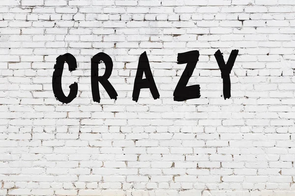 Слово "сумасшедший" написано на стене из белого кирпича — стоковое фото