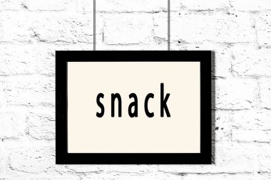 Beyaz tuğla duvarda asılı siyah çerçeve ve abur cubur.