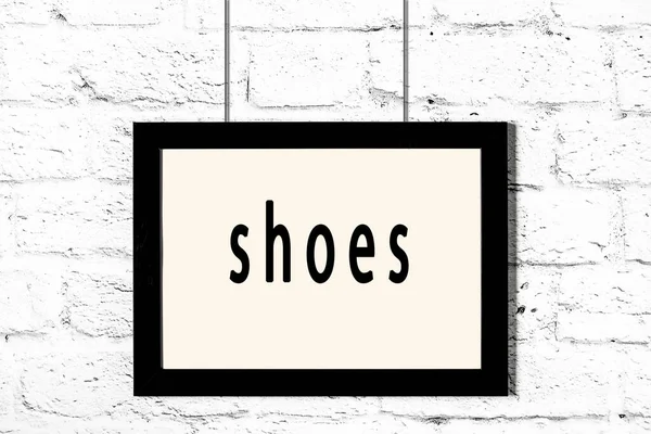 Černý rám zavěšený na bílé cihlové zdi s nápisem boty — Stock fotografie
