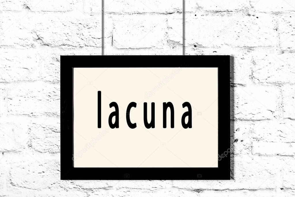 Black frame hanging on white brick wall with inscription lacuna
