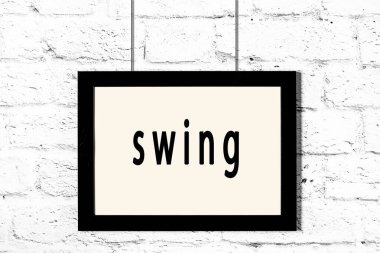 Beyaz tuğla duvarda asılı siyah çerçeve ve yazı salıncak