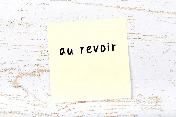 Gele plakkerige noot op houten muur met handgeschreven woord au revoir — Stockfoto