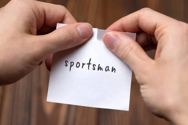 Mãos de um homem rasgando um pedaço de papel com inscrição desportista — Fotografia de Stock