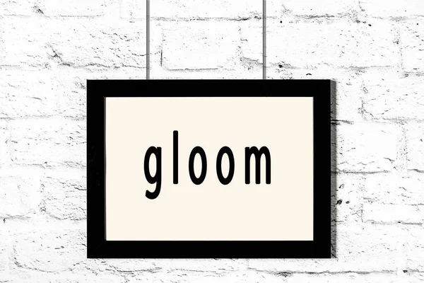 Quadro preto pendurado na parede de tijolo branco com gloom inscrição — Fotografia de Stock