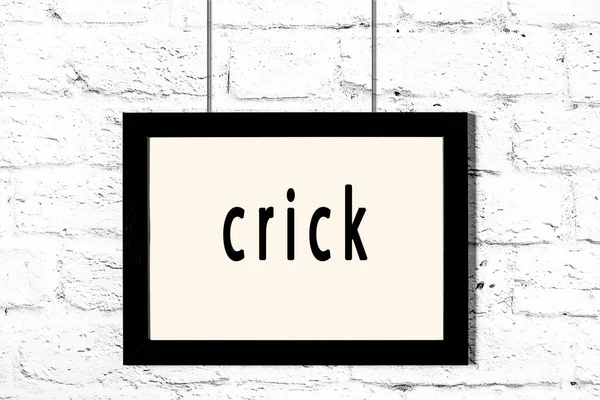 Zwart frame opknoping op witte bakstenen muur met inscriptie crick — Stockfoto