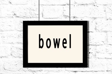 Siyah çerçeve beyaz tuğla duvarda asılı ve bağırsağında yazı var.