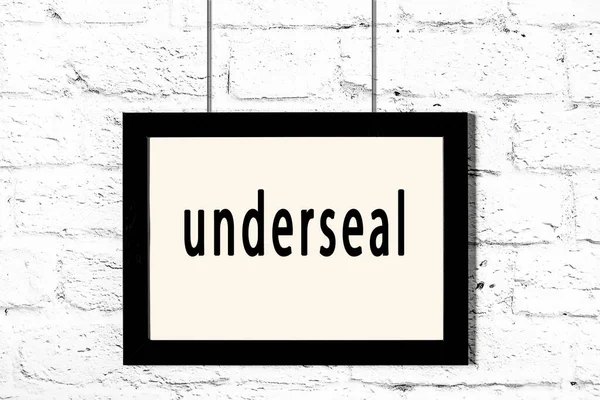 Quadro preto pendurado na parede de tijolo branco com inscrição underseal — Fotografia de Stock