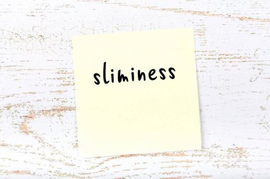 Tahta duvardaki sarı yapışkan notta elle yazılmış ince kelimeler var.