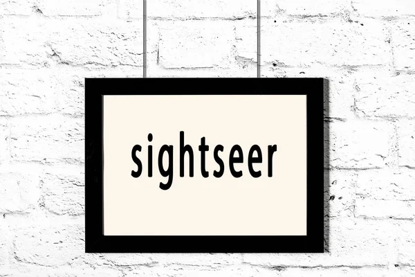 Black frame hanging on white brick wall with inscription sightseer — Stock Photo, Image