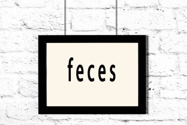 Beyaz tuğla duvarda asılı siyah çerçeve ve yazılı dışkı.