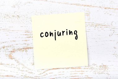 Tahta duvarda sarı yapışkan bir not ve el yazısıyla yazılmış bir büyü.