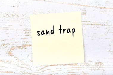 Tahta duvarda el yazısı kum tuzağı olan sarı yapışkan bir not.