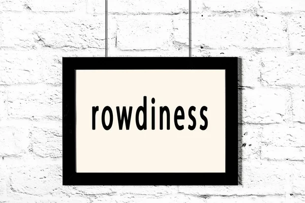 Schwarzer Rahmen hängt an weißer Ziegelwand mit Inschrift Rowdyness — Stockfoto