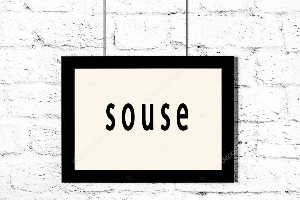 Black frame hanging on white brick wall with inscription souse