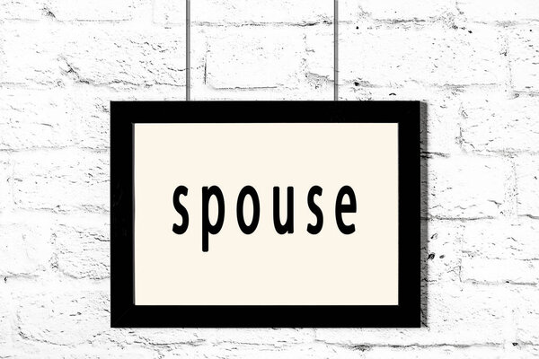 Черная рамка висит на стене из белого кирпича с надписью супруг
