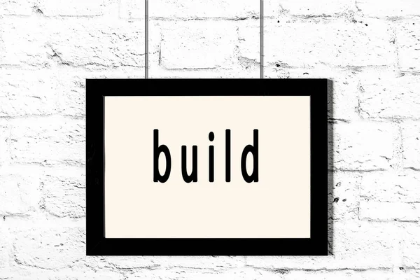 Czarna ramka wisząca na białej ceglanej ścianie z napisem build — Zdjęcie stockowe