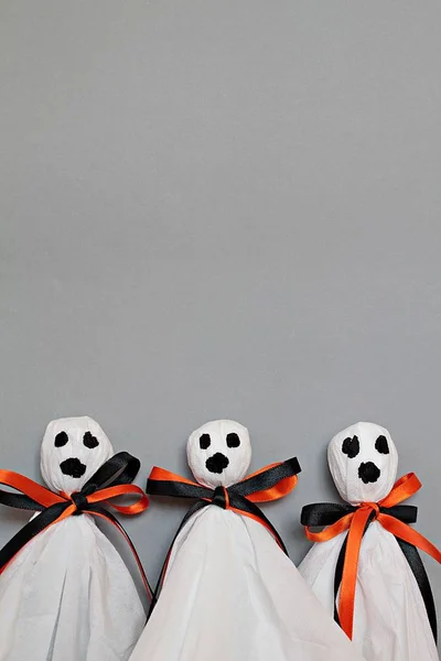 Three halloween ghosts DIY made from white tissue paper, black and orange ribbon on gray background