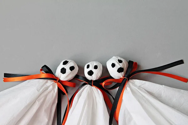 Three halloween ghosts DIY made from white tissue paper, black and orange ribbon on gray background