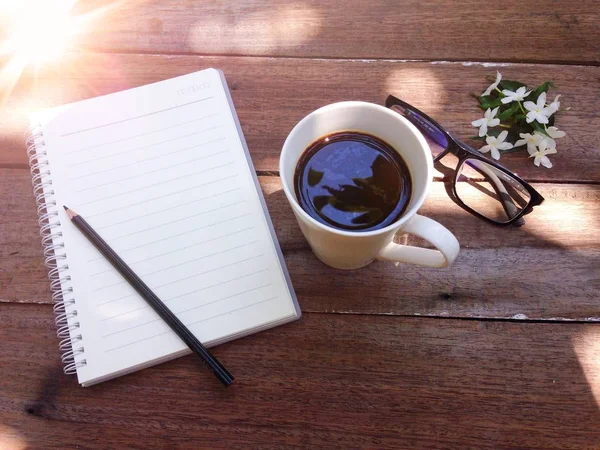 Tasse de café, verres, papier pour ordinateur portable, crayon et fleurs blanches sur fond bois et fusée éclairante — Photo