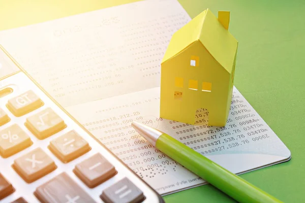 Spaarrekening passbook, rekenmachine, pen en geel papier huis op groene achtergrond — Stockfoto