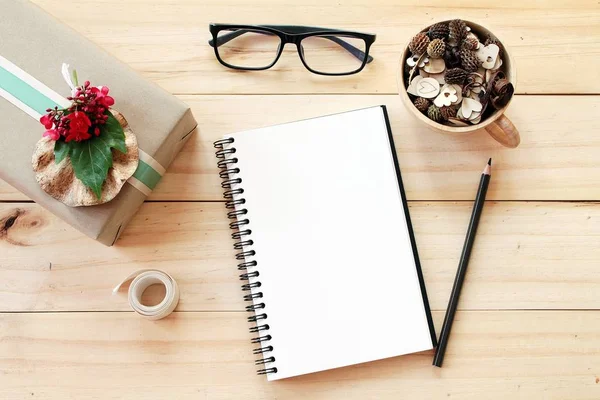 Escritorio de espacio de trabajo con cuaderno, lápiz, conos de pino en taza de madera de té, gafas, caja de regalo y cinta sobre fondo de madera — Foto de Stock