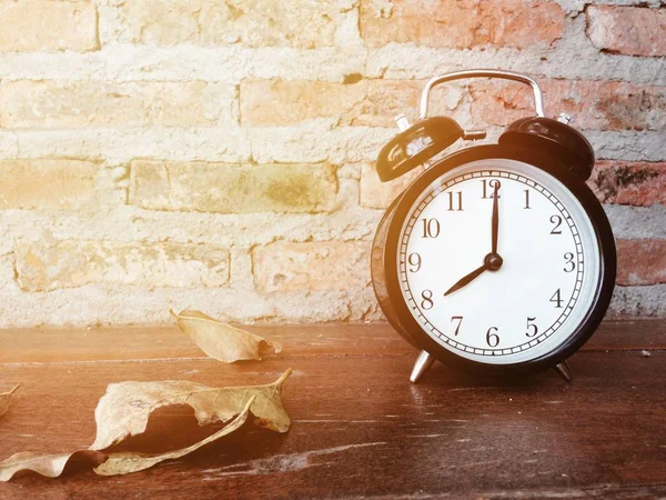 Relógio de alarme preto retro e folhas secas na mesa de madeira — Fotografia de Stock