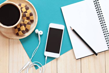 Ahşap arka planda kalem, cep telefonu, kurabiye ve kahve fincanı ile boş defter ile çalışma masası üst görünümü