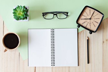 Ahşap arka plan üzerine kalem, kahve fincanı, gözlük, retro çalar saat ve bitki ile boş defter ile çalışma masası üst görünümü
