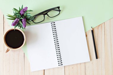 Ahşap arka plan üzerine kalem, kahve fincanı, gözlük ve bitki ile boş defter ile çalışma masası üst görünümü