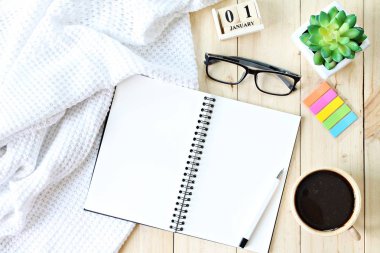 Yat veya battaniye, Açık boş defter kağıt, kahve fincanı ve yeni yıl küp takvim ahşap arka plan üzerinde beyaz üstten görünüm örme