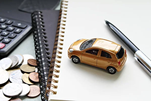 Miniature car model, pen, notebook papers, calculator and coins on office table