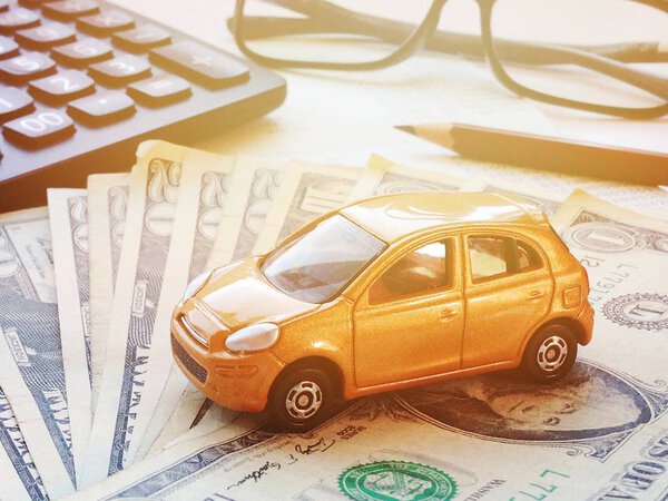 Миниатюрные модели автомобилей, калькулятор, долларовые деньги и сберегательная книжка или финансовая отчетность на столе офиса
