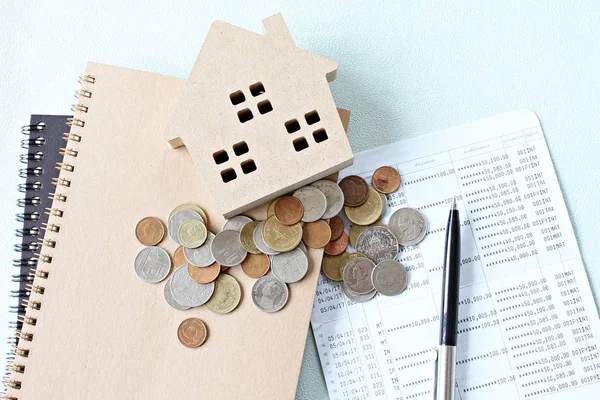 Modo de casa de madera, monedas y libro de cuentas de ahorro o estado financiero en la mesa de escritorio —  Fotos de Stock