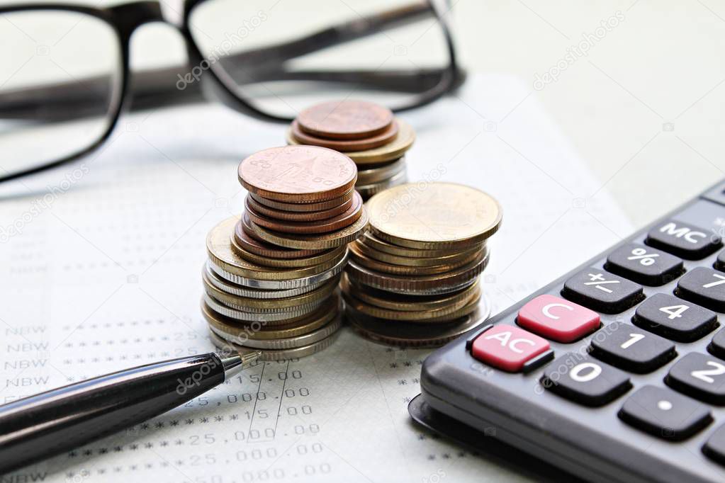 Coins stack, calculator, pen, eyeglasses and saving account book or financial statement on office desk table