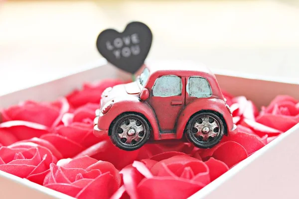 Business, finance, car loan, love, gifts or Valentine\'s day concept : Miniature car model with love you on heart tag and red roses box on red background