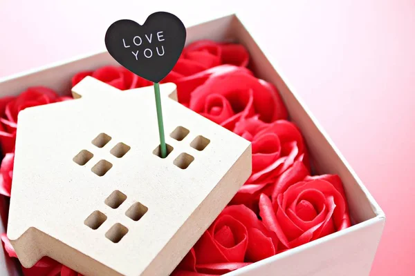 Business, finance, property ladder, mortgage loan, love, gifts or Valentine\'s day concept : Wood house model with love you tag and red roses on red background with copy space for adding or mock up