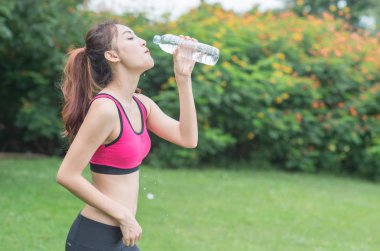 genç çekici kadın içme suyu parkta plastik şişe