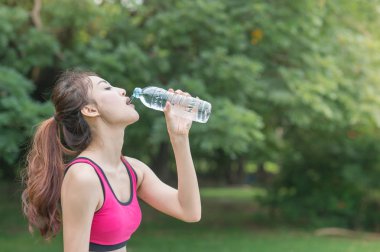 genç çekici kadın içme suyu parkta plastik şişe