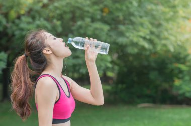 genç çekici kadın içme suyu parkta plastik şişe