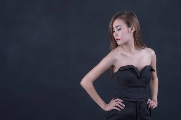 Beautiful sexy woman with perfect slim body and long curly hair in black dress posing over black background. Studio shot. — Stock Photo, Image