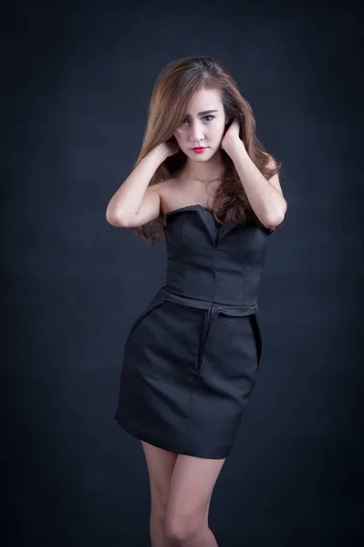 Hermosa mujer sexy con cuerpo delgado perfecto y pelo rizado largo en vestido negro posando sobre fondo negro. Captura de estudio . —  Fotos de Stock