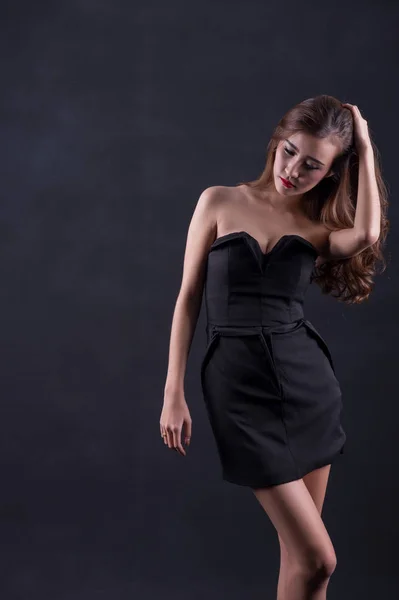Hermosa mujer sexy con cuerpo delgado perfecto y pelo rizado largo en vestido negro posando sobre fondo negro. Captura de estudio . —  Fotos de Stock