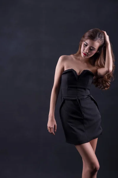 Bella donna sexy con perfetto corpo sottile e lunghi capelli ricci in abito nero in posa su sfondo nero. Studio girato . — Foto Stock