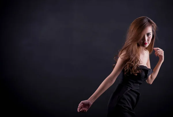 Сексуальная женщина с идеально стройным телом и длинными кудрявыми волосами в черном платье позирует на черном фоне. Снимок студии . — стоковое фото