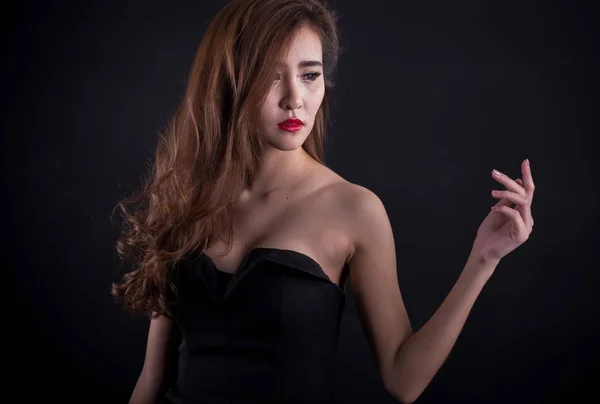 Όμορφη σέξι γυναίκα με τέλειο λεπτό σώμα και μακριά σγουρά μαλλιά σε μαύρο φόρεμα που παρουσιάζουν πάνω από το μαύρο φόντο. Studio που γυρίστηκε. — Φωτογραφία Αρχείου