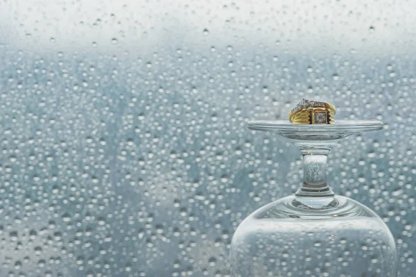 Anillo de boda en copa de champán delante del espejo con gotas de lluvia . Fotos de stock libres de derechos