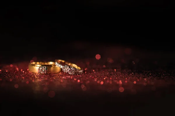 Kırmızı parlak ve siyah arka plan üzerinde kırmızı bokeh ile altın alyans.