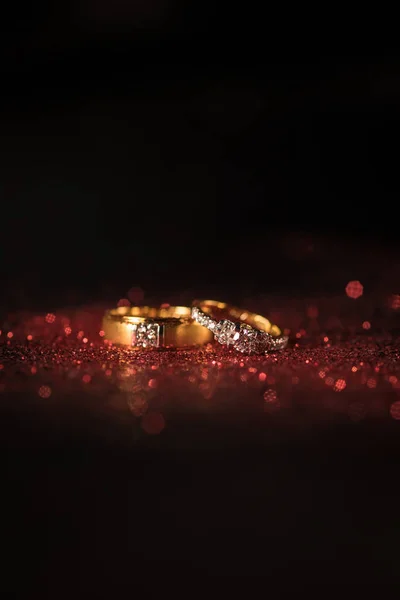 Kırmızı parlak ve siyah arka plan üzerinde kırmızı bokeh ile altın alyans.