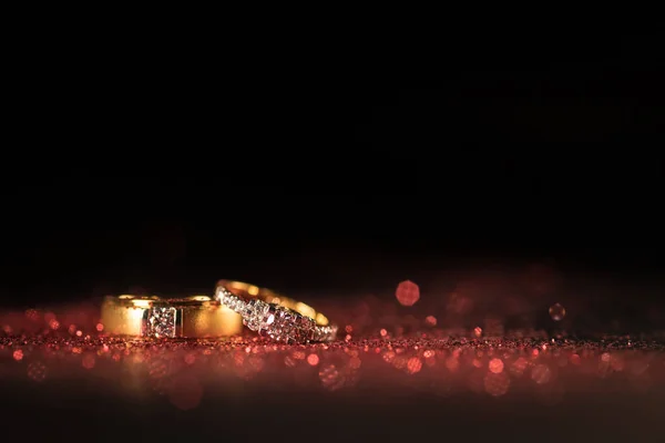 Kırmızı parlak ve siyah arka plan üzerinde kırmızı bokeh ile altın alyans.